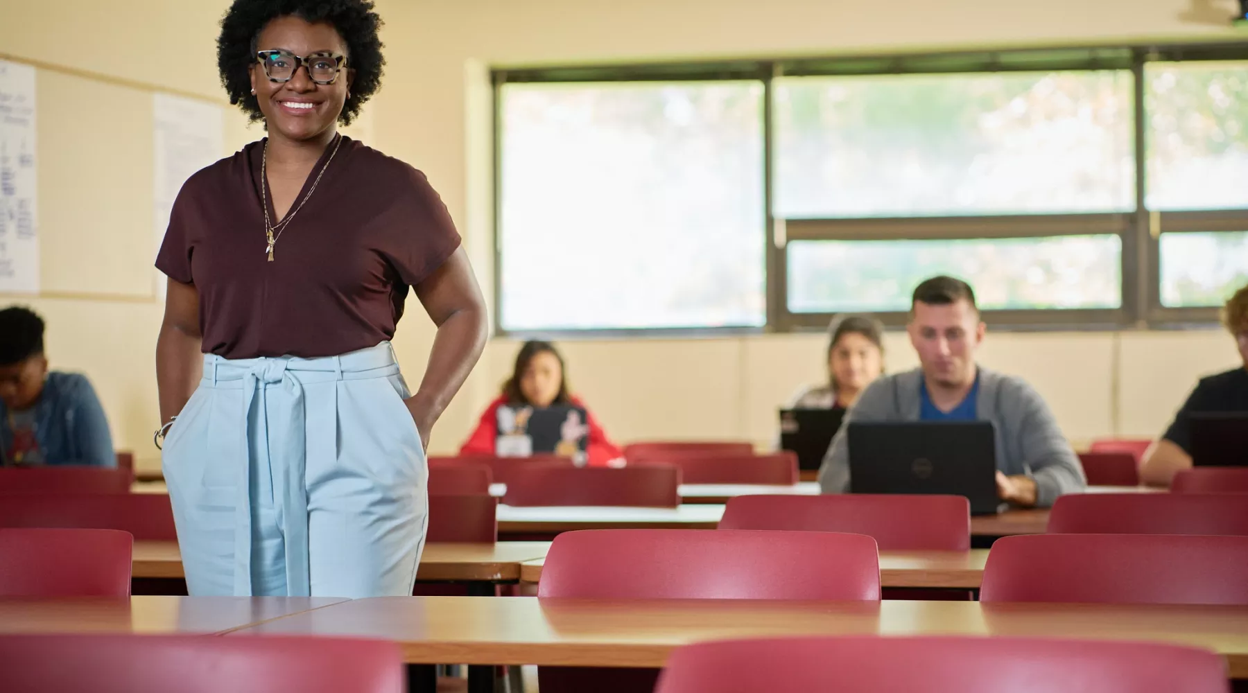 Female professor stands in front of her classroom and students posing for the campaign.