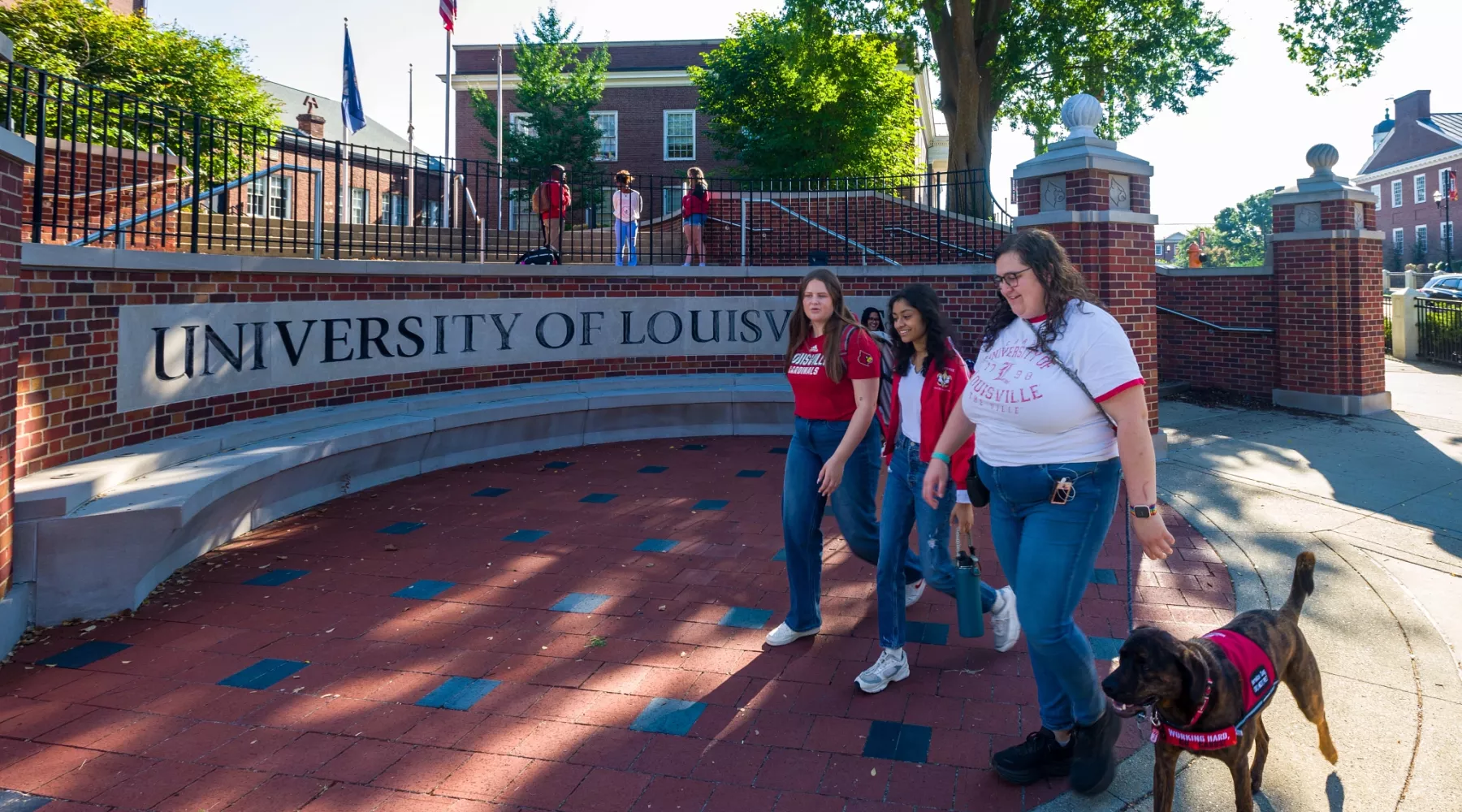 Three students walking near a UofL sign on Belknap campus